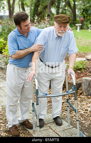 Ältere Mann sieht traurig als er kämpft, um seinen erwachsenen Sohn gehen mit einer Gehhilfe hilft ihm Stockfoto