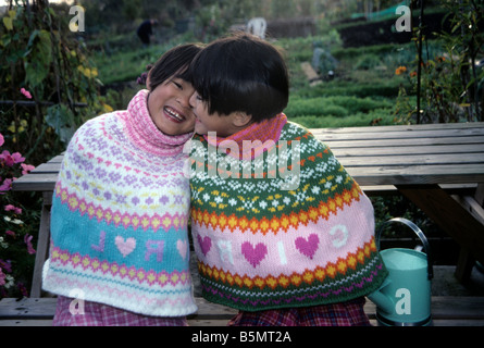 Chinesische Zwillingsmädchen kuscheln miteinander in einem englischen Garten Stockfoto