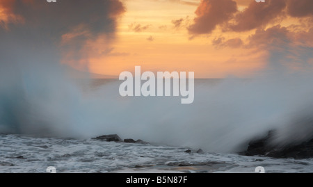 Wellen, die auf Felsen bei Sonnenuntergang Stockfoto