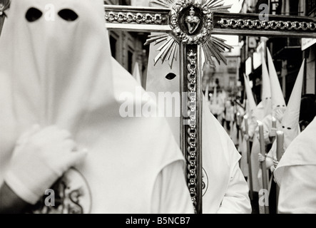 Mitglieder der Bruderschaft in ihre Masken und Kostüme tragen ein Kreuz während der Semana Santa Prozessionen durch die Straßen. Stockfoto