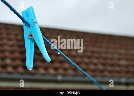 Eine blaue Pflock auf eine Wäscheleine im Regen mit einem Garagendach im Hintergrund Stockfoto