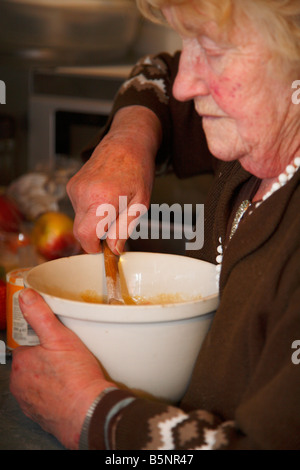 Alte Frau mit Schüssel Zutaten mit einem Kochlöffel rühren. Stockfoto