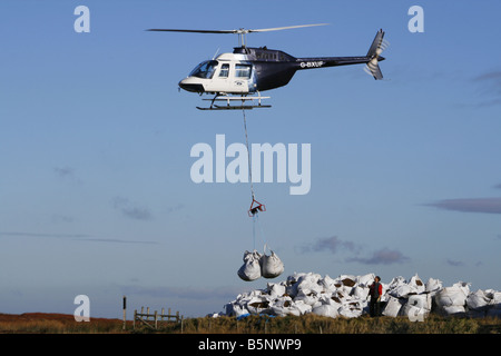 Helikopter-Hebekissen von Samen beladen Kompost für die Arbeiter, die Regeneration der Heide in der Nähe von Torside Reservoir in High Peak. Stockfoto