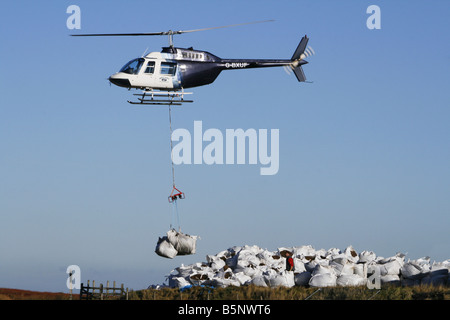 Helikopter-Hebekissen von Samen beladen Kompost für die Arbeiter, die Regeneration der Heide in der Nähe von Torside Reservoir in High Peak. Stockfoto