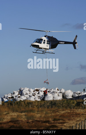 Helikopter-Hebekissen von Samen beladen Kompost für die Arbeiter, die Regeneration der Heide in der Nähe von Torside Reservoir in High Peak. Stockfoto