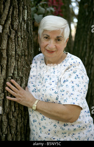 Eine attraktive ältere Dame lehnte sich gegen einen Baum im park Stockfoto