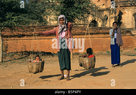 Eine burmesische Frau trägt ihre beiden Kinder in Körben vor dem Tayok Pye Tempel in Bagan, Burma bzw. Myanmar Stockfoto