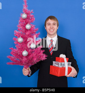 Junger Mann Betrieb rosa Weihnachtsbaum und verpackte Geschenke Stockfoto