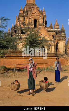 Eine burmesische Frau trägt ihre beiden Kinder in Körben vor dem Tayok Pye Tempel in Bagan, Burma bzw. Myanmar Stockfoto