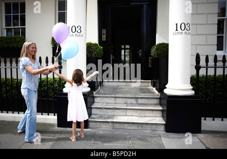 Junge Mädchen und Mutter binden Geburtstag Party Luftballons zu Geländer von ihrem makellosen Haus in Belgravia, London Stockfoto