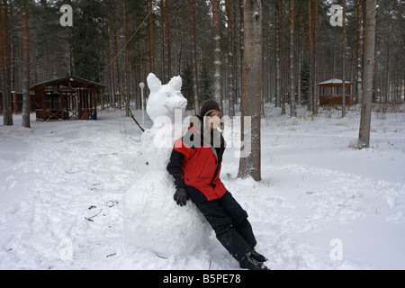 Winterspaß: lächelnde Frau mit Schneemann auf Winter-Wald-Hintergrund Stockfoto