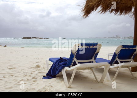 Beach Lounge Stühle sitzen am Ufer des karibischen Ozean in Cancun Mexiko mit stürmischen Himmel und Palapa leer Stockfoto