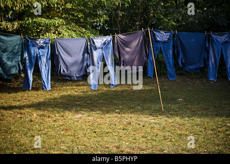 Blaue Jeans und Hemden hängen an einer Wäscheleine draußen in der Sonne zu arbeiten. Stockfoto