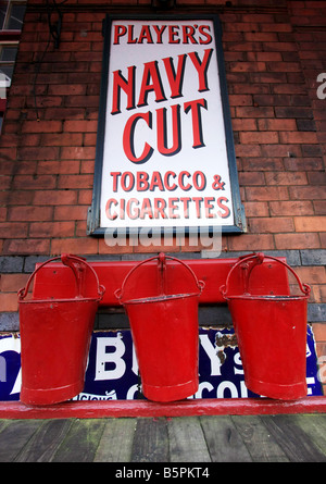 Drei 3 alte altmodische rotes Feuer Eimer unter eine alte Emailleschild Werbung Spieler Navy Cut Zigaretten Stockfoto
