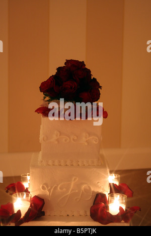 Eine ausgefallene Hochzeitstorte mit roten Rosen und Kerzen brennen um den Kuchen für eine Hochzeitsfeier angezeigt Stockfoto