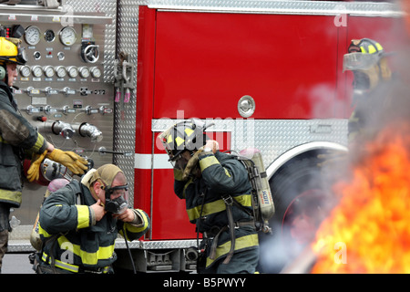 Vier Feuerwehrleute immer ein Neuanschluß bereit aus einem Feuerwehrauto bei einer Feuer-Demonstration auf einem Feuer Sicherheit Messe Stockfoto