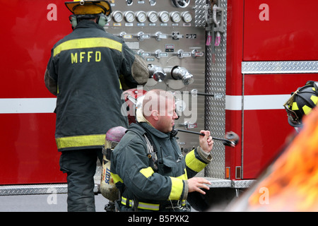 Drei Feuerwehrleute immer bereit vor einem Feuerwehrauto, ein Feuer zu bekämpfen Stockfoto