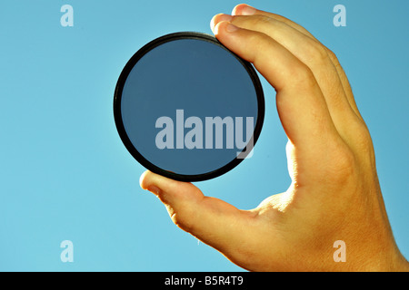 Blick auf Himmel durch einen kreisförmigen Polarisator Filter von einer männlichen Hand Wabbel Stockfoto
