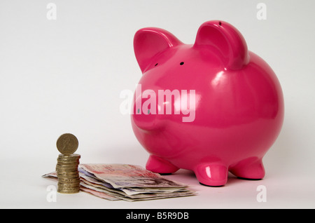 eine halbe Seitenprofil ein rosa Schweinchen bank mit einem Haufen von Münzen und britische Banknoten vor es Stockfoto