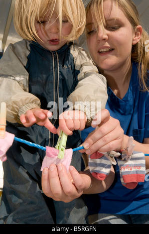 junges Mädchen anheften pegging Socken an Wäscheleine von Kindergarten Arbeitnehmerin in einer Betreuungseinrichtung Kindergarten UK geholfen Stockfoto