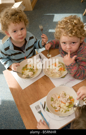 drei junge Pre-Schulkinder im Kindergarten Kindertagesstätte mit ihren Mittag essen Huhn Eintopf, sitzen Couchtische, UK Stockfoto