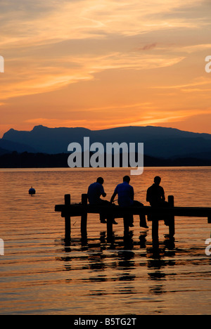 Drei Jungs sitzen auf einem Steg und Angeln bei Sonnenuntergang, Lake Windermere, englischen Lake District Stockfoto