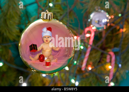 Ein kleines Mädchen, gekleidet in eine Weihnachtsmann-Mütze spiegelt sich in einer Christbaumkugel auf einen Weihnachtsbaum mit Lichtern und Zuckerstangen Stockfoto