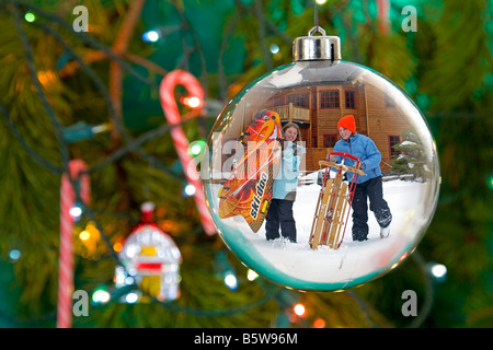 Zwei Mädchen mit Schlitten eine Christbaumkugel auf einen Weihnachtsbaum mit Zuckerstangen an Heiligabend spiegeln sich in Stockfoto