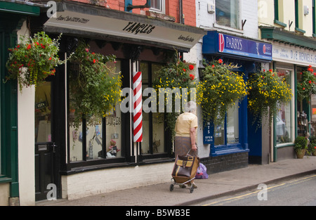 Ältere Dame mit Einkaufswagen vorbei an Ladenzeile im Marktflecken UK Stockfoto