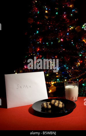 Kinder-Brief an den Weihnachtsmann ausgelassen am Heiligabend mit Keksen und Glas Milch vor dem Weihnachtsbaum Stockfoto