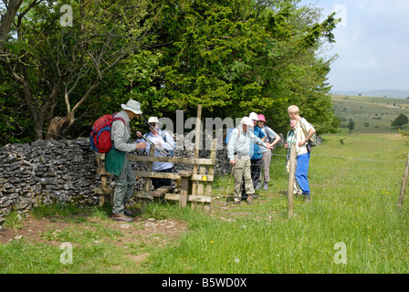 Gruppe von älteren Wanderer, die Verhandlungen über einen Stil in einem Drahtzaun neben einer Trockensteinmauer englischen Lake District Stockfoto