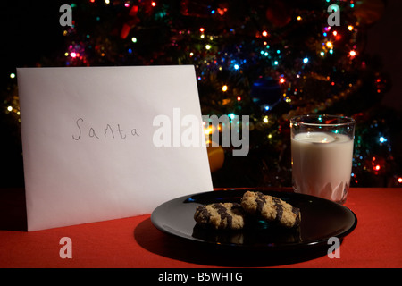 Kinder-Brief an den Weihnachtsmann ausgelassen am Heiligabend mit Keksen und Glas Milch vor dem Weihnachtsbaum Stockfoto