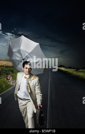 Geschäftsmann hält einen Regenschirm und zu Fuß auf der Straße Stockfoto