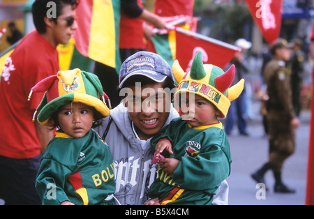 Mann, der seine Kinder in Nationalmannschaftstrikots und Hüten in bolivianischen Farben beim internationalen Fußballspiel La Paz, Bolivien, hält Stockfoto