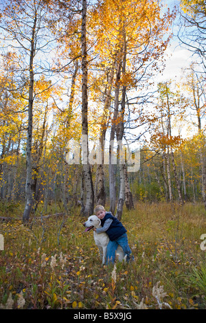 kleiner Junge umarmt seinen Hund unter Espen im Herbst Stockfoto