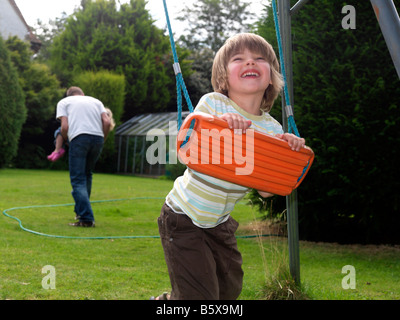 Vier Jahre alter Junge spielt mit Swing in einem Garten-Surrey Stockfoto