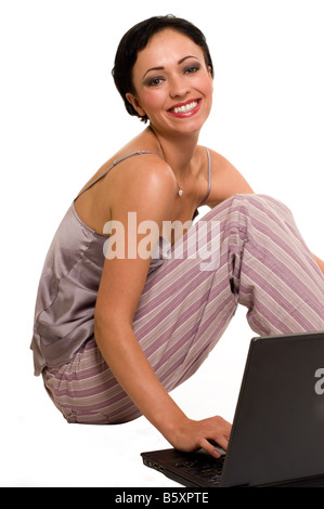 Attraktive kurze Haare brünett tragenden Pyjamas auf weiß sitzend mit Laptop Lachen Ausdruck Stockfoto