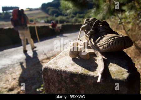 Pilger pass ein Schuh und ein paar Steine auf einem Kilometer Markierung entlang des Camino de Santiago zwischen Sarria und Portomarin, Galizien, Spanien links Stockfoto