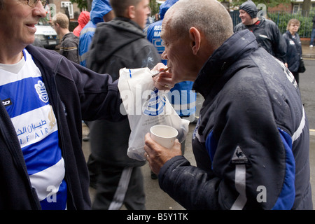 Ein männlicher Fan QPR zündet sich seine Freunde Zigarette vor einem Spiel an der Loftus Road. Stockfoto