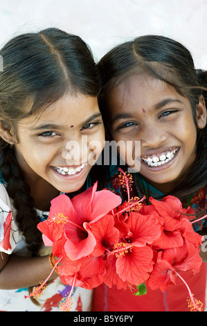 Zwei indische Mädchen halten rote Hibiskusblüten.  Andhra Pradesh, Indien Stockfoto