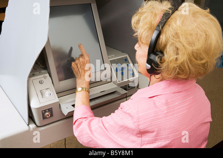 Ältere Dame Kopfhörer für Hörgeschädigte und Abstimmung über Bildschirm Maschine Touch Stockfoto