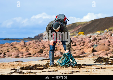 Mann mit Rucksack auf dem Rücken aufrollen etwas blauem blauen Seil, das am Slaggan Strand angespült worden ist Stockfoto