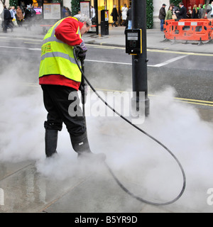 Ein Arbeiter des Gemeinderats, der eine Warnweste trägt, reinigt klebrige Kaugummikautschukteile von Gehwegen in Oxford Street West End London, England Stockfoto