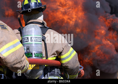 Feuerwehrleute vor einem lodernden Feuer Inferno die Wasser-Schlauchleitung Verwendung vorbereiten Stockfoto