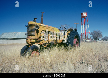 Eine alten Bauernhof Traktor sitzt in einem Feld unter einem Wasserturm in der Nähe von der kleinen nordöstlichen Stadt von Roy New Mexico verlassen Stockfoto