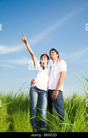 junges Paar in der Wiese mit Hand in Luft umarmt und lächelnd Textfreiraum Stockfoto