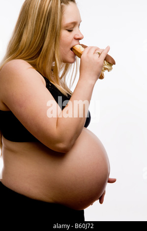 hochschwangere blonde Britin Essen eine Creme gefüllt Schokolade Eclair Kuchen spät in ihr prengancy Stockfoto