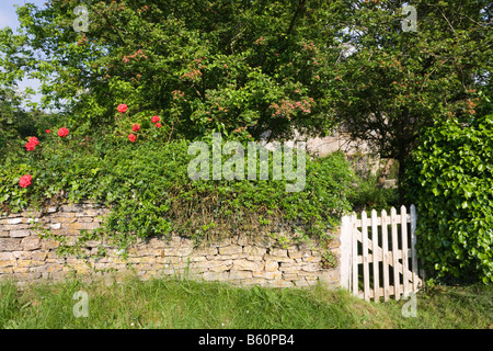 Die Gartenmauer runden ein rustikalen Landhaus aus Stein in der Cotswold-Dorf Swinbrook, Oxfordshire Stockfoto