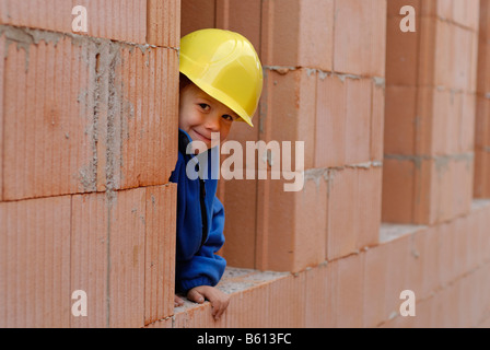 Kleiner Junge trägt einen gelben Schutzhelm lächelnd an einem Hausbau Stockfoto