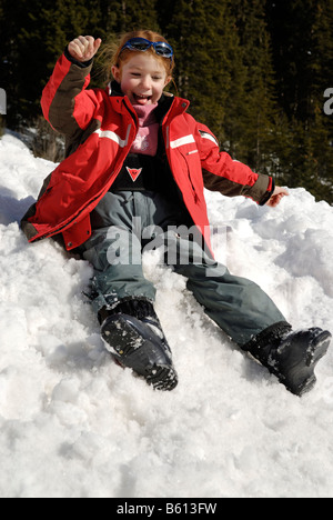 Lachende Mädchen schleudern unten einen schneebedeckten Hügel, spielen im Schnee Stockfoto